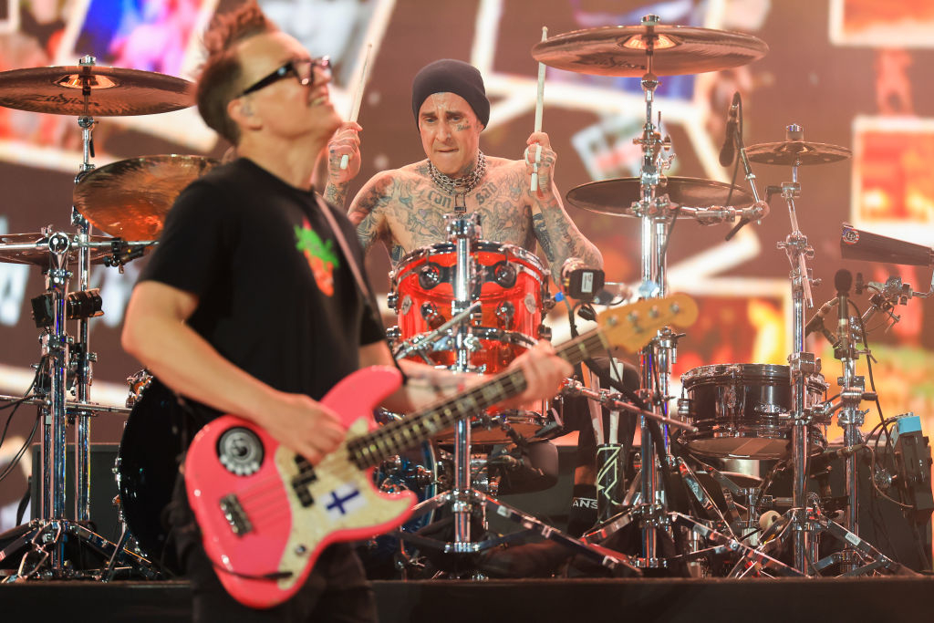 Mark Hoppus and Travis Barker performing with photographs on a screen behind them.