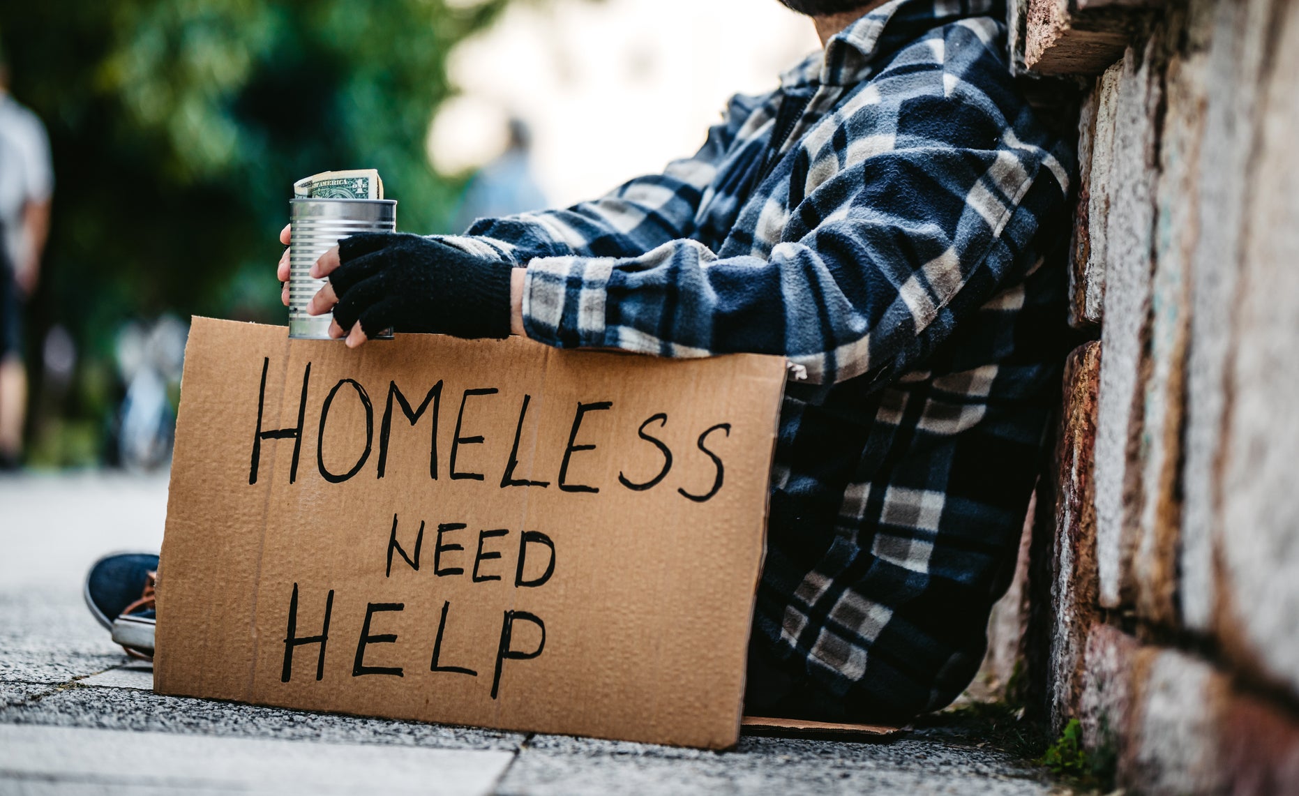 A person sitting on the street and holding a sign, &quot;Homeless need help&quot;