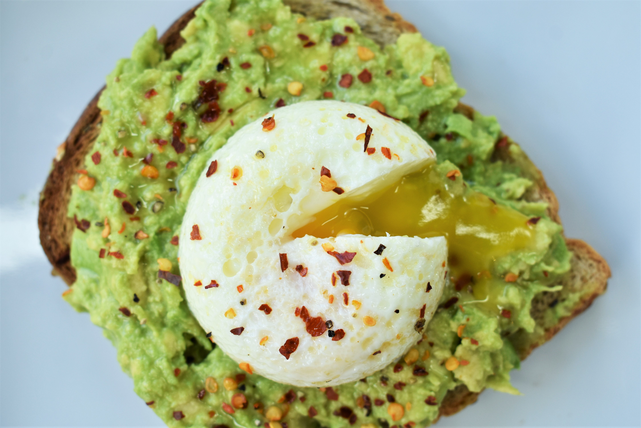 A runny egg sits on top of avocado toast