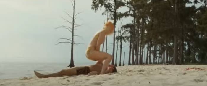 Nicole in a bikini squatting over Zac in swim trunks on a beach
