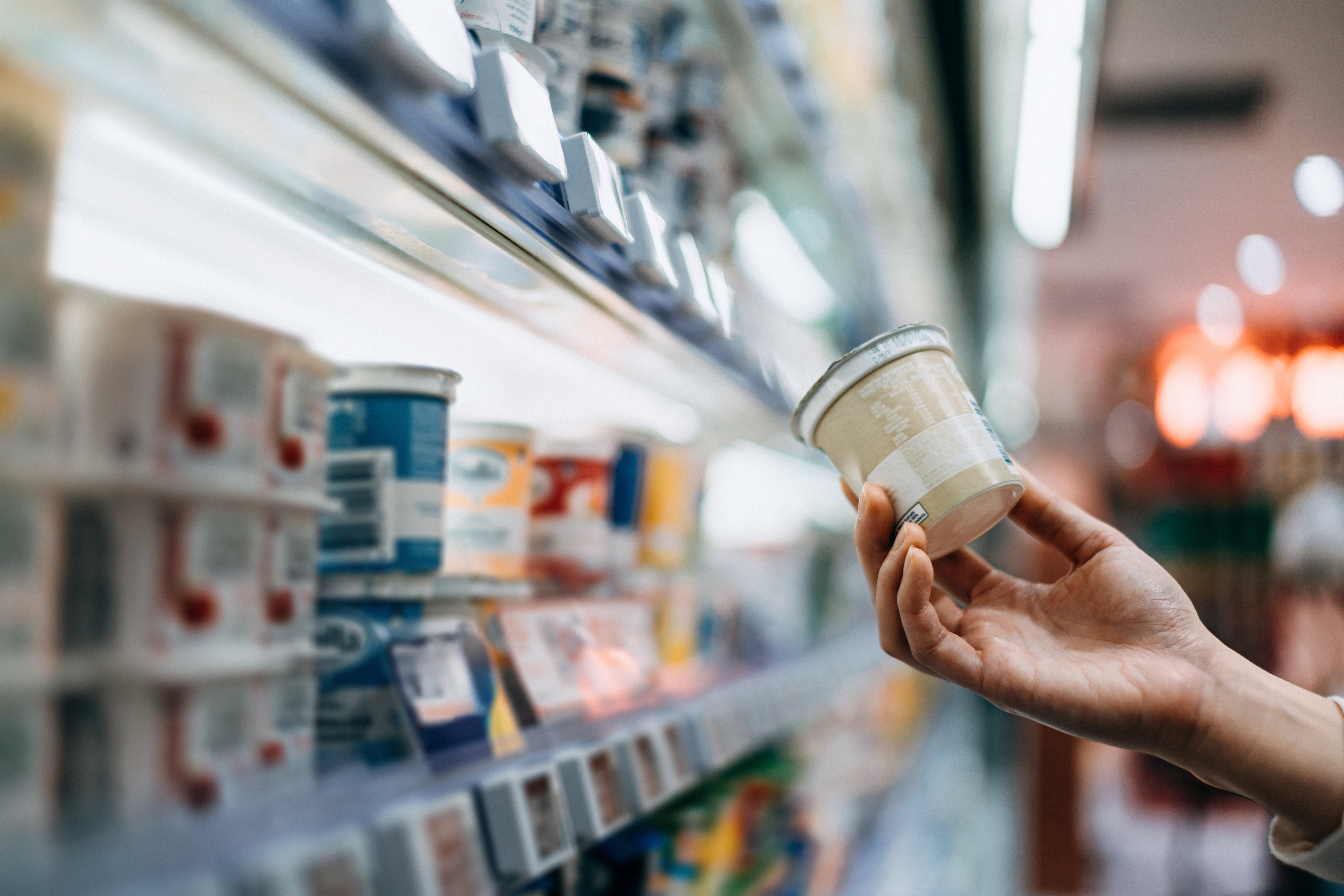 Close-up of a woman&#x27;s hand shopping for fresh organic healthy yogurt along the dairy aisle in supermarket