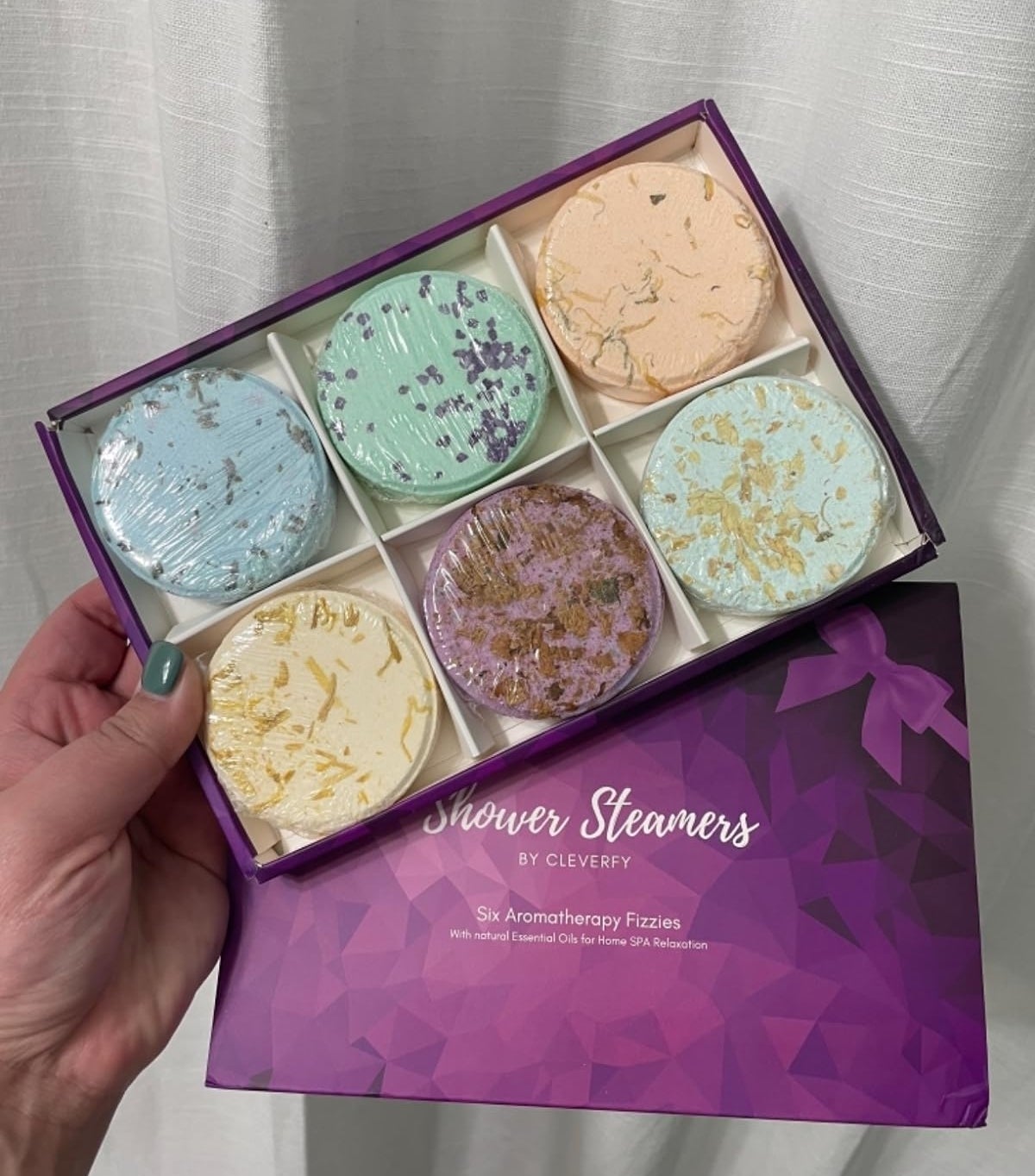 Hand holding a box of six shower steamers with various textures, labeled &quot;Shower Streamers by Clevery.&quot;