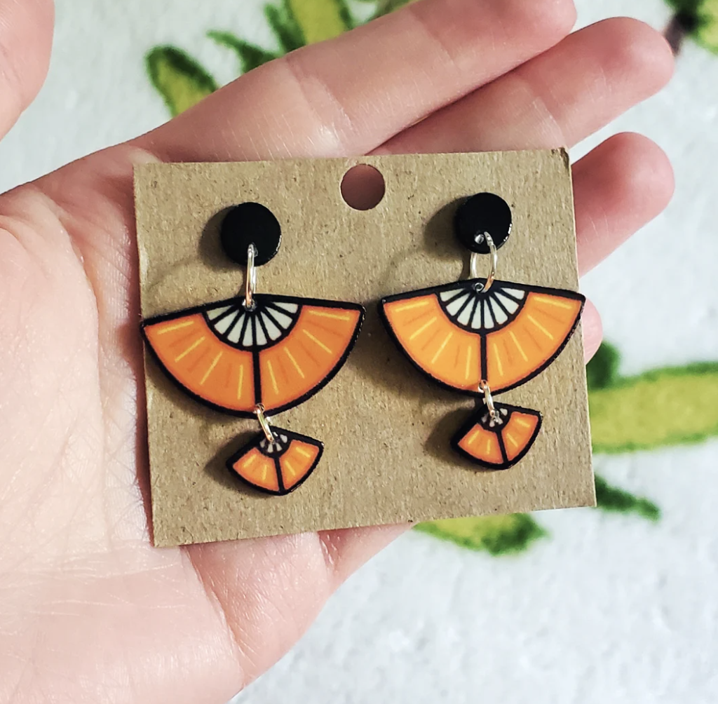 Hand holding a set of orange staff glider earrings