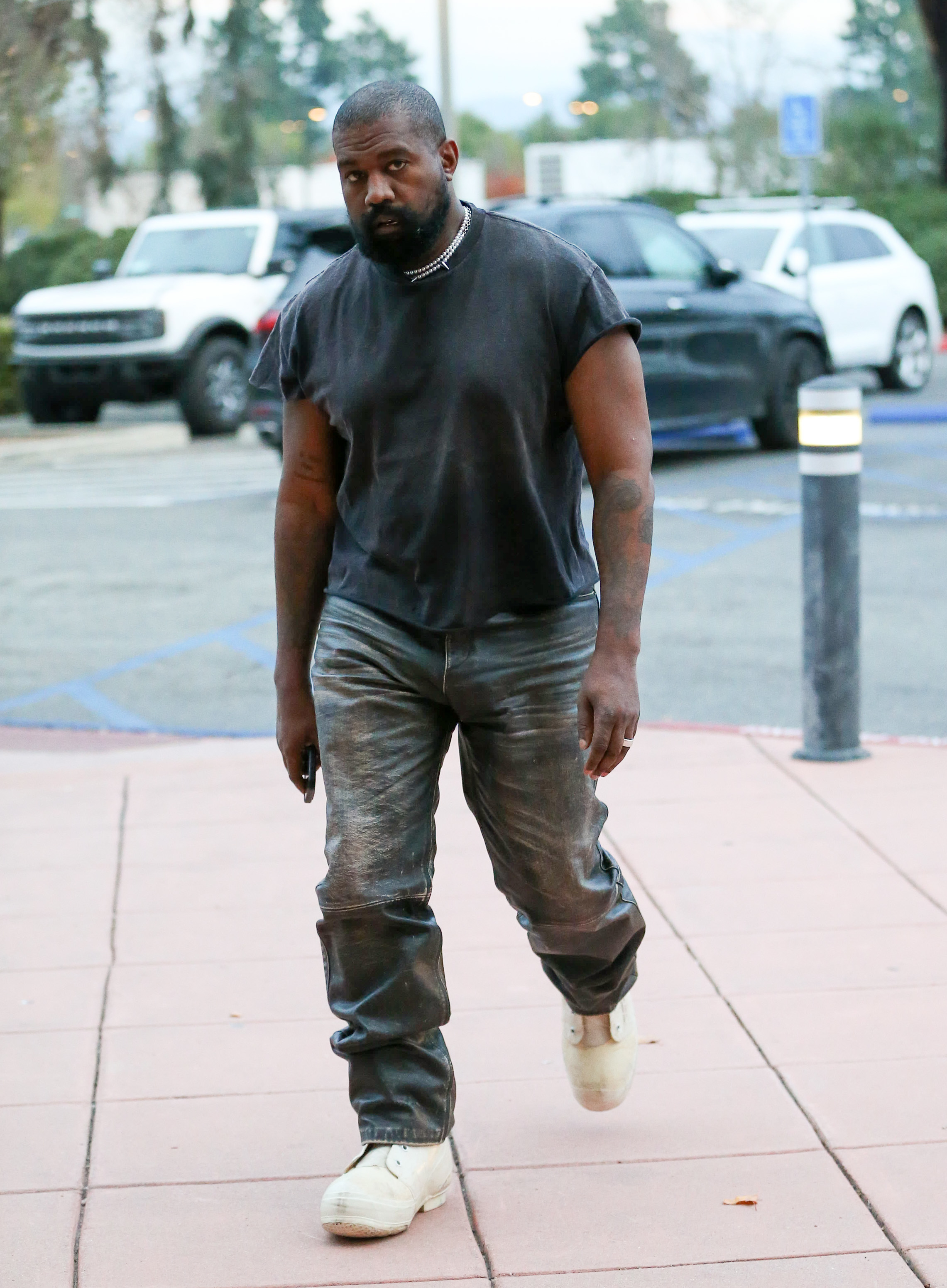 Close-up of Ye in pants and a T-shirt walking on the street by a parking lot