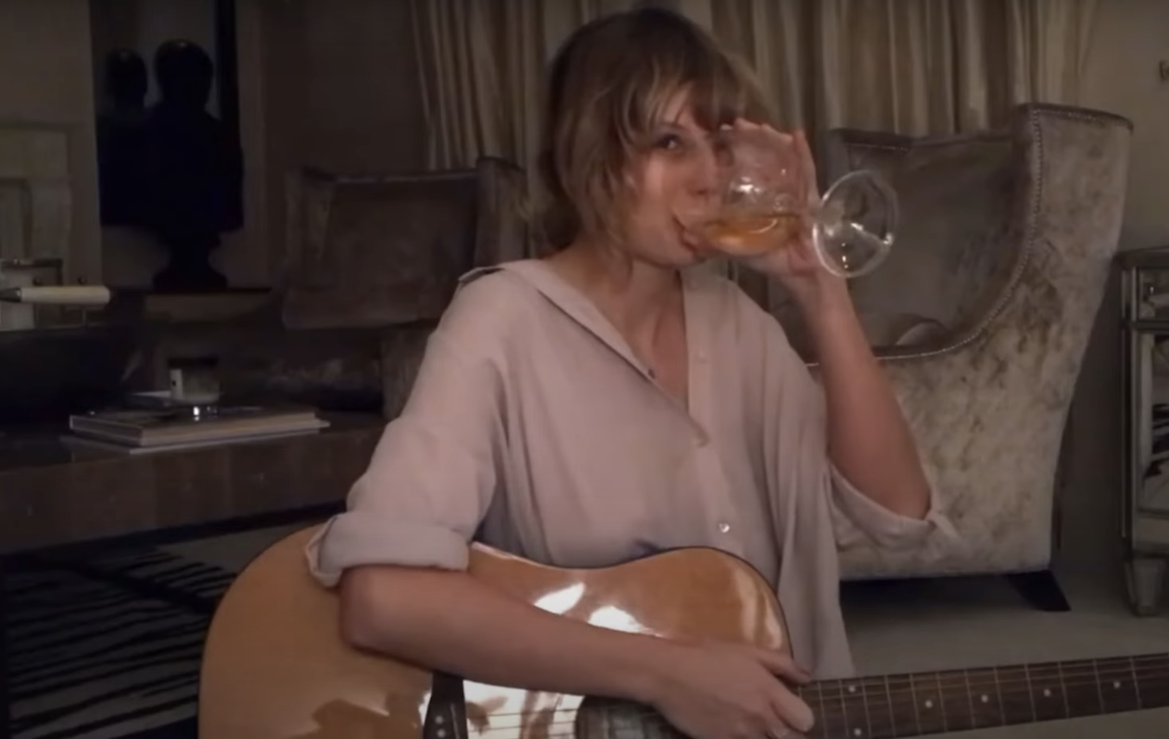 Close-up of Taylor drinking from a wine glass and holding a guitar