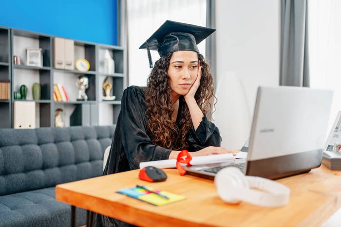 girl wearing graduation gown with a sad look and on her computer