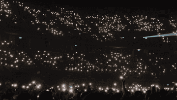 Audience holding up lit mobile phones at a concert, creating a starry effect indoors