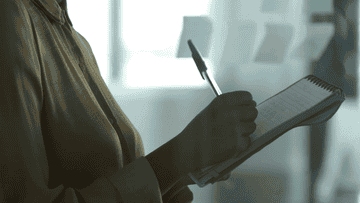 Person holding pen and notepad, preparing to write, with a blurred background