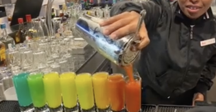 Bartender pouring drinks into glasses, from blue to green to yellow to orange