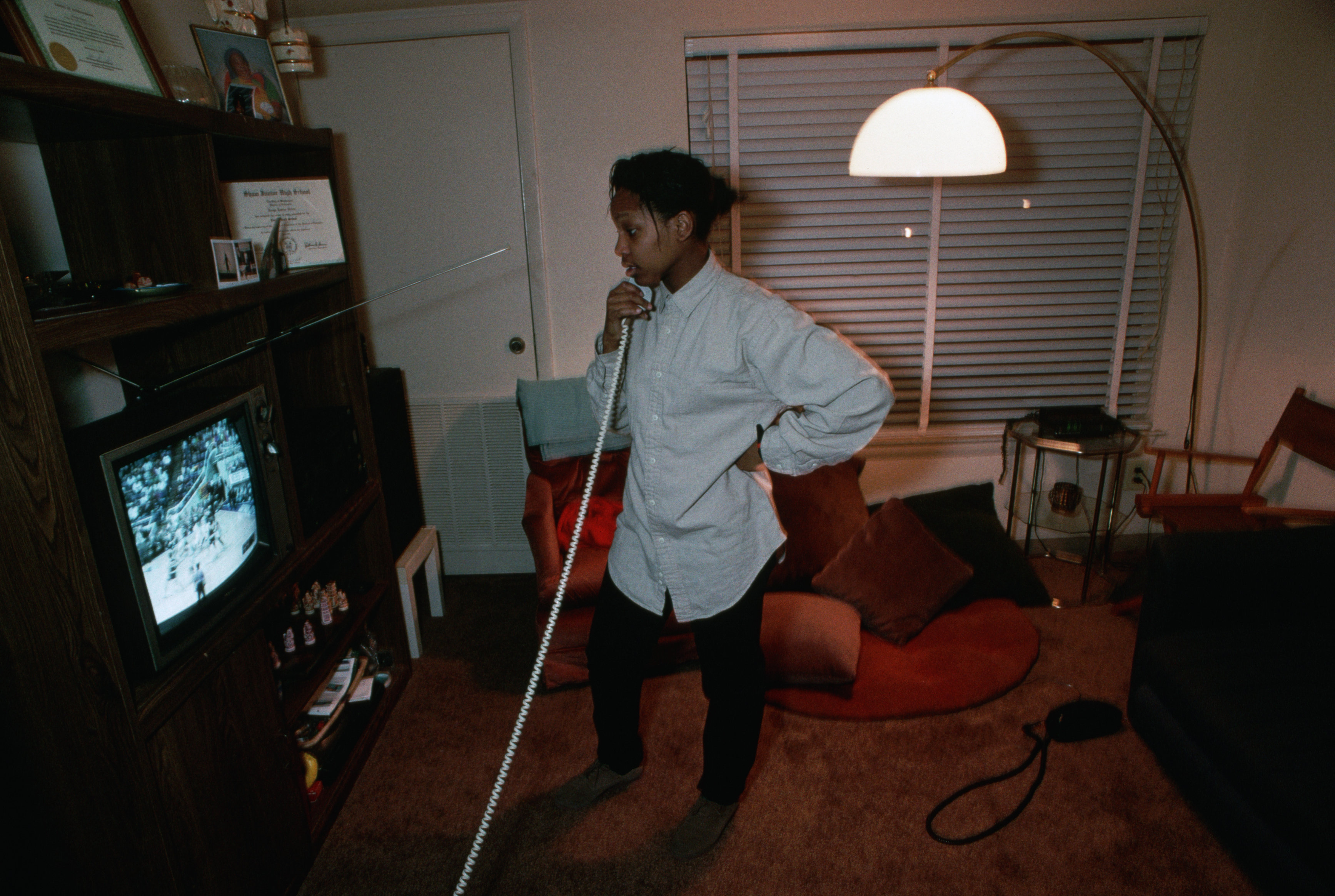 A woman is talking on a corded phone while watching TV