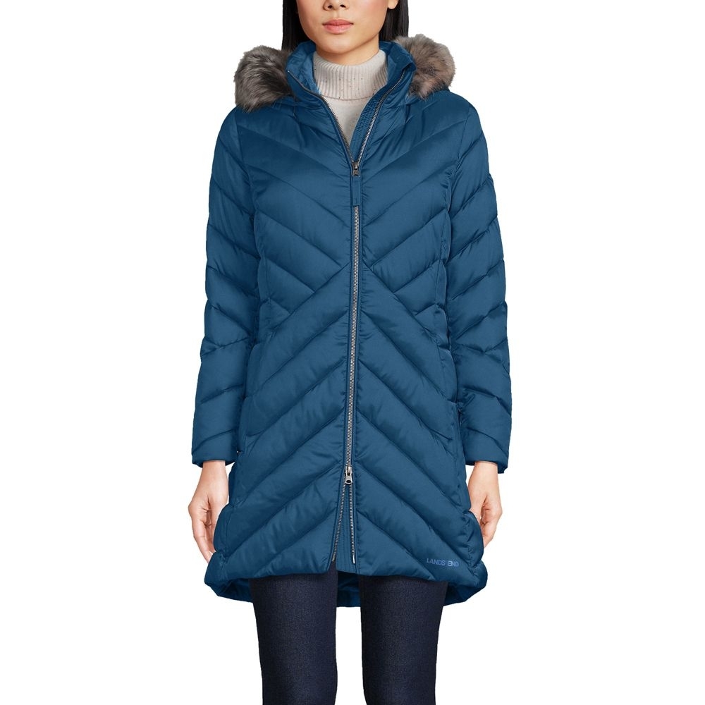 a person wearing a long dark blue zip-up insulated coat with angled quilting and a faux fur trimmed hood