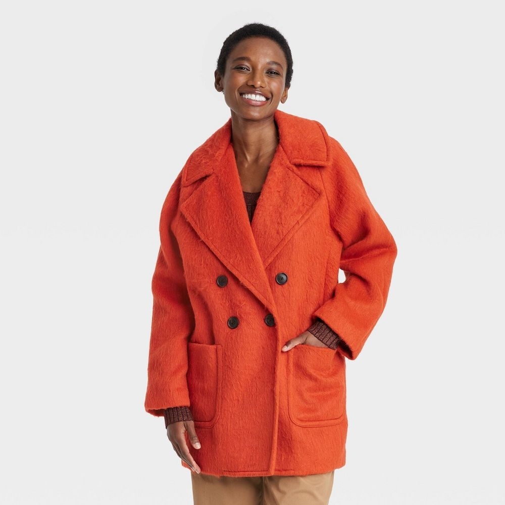 a person wearing an oversized orange fuzzy lapel coat with very large front pockets