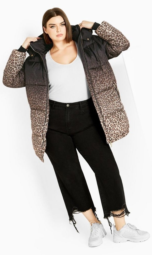 a person wearing a hoodless puffer coat that is black around the neckline, and ombre-fades into leopard print in the body of the coat