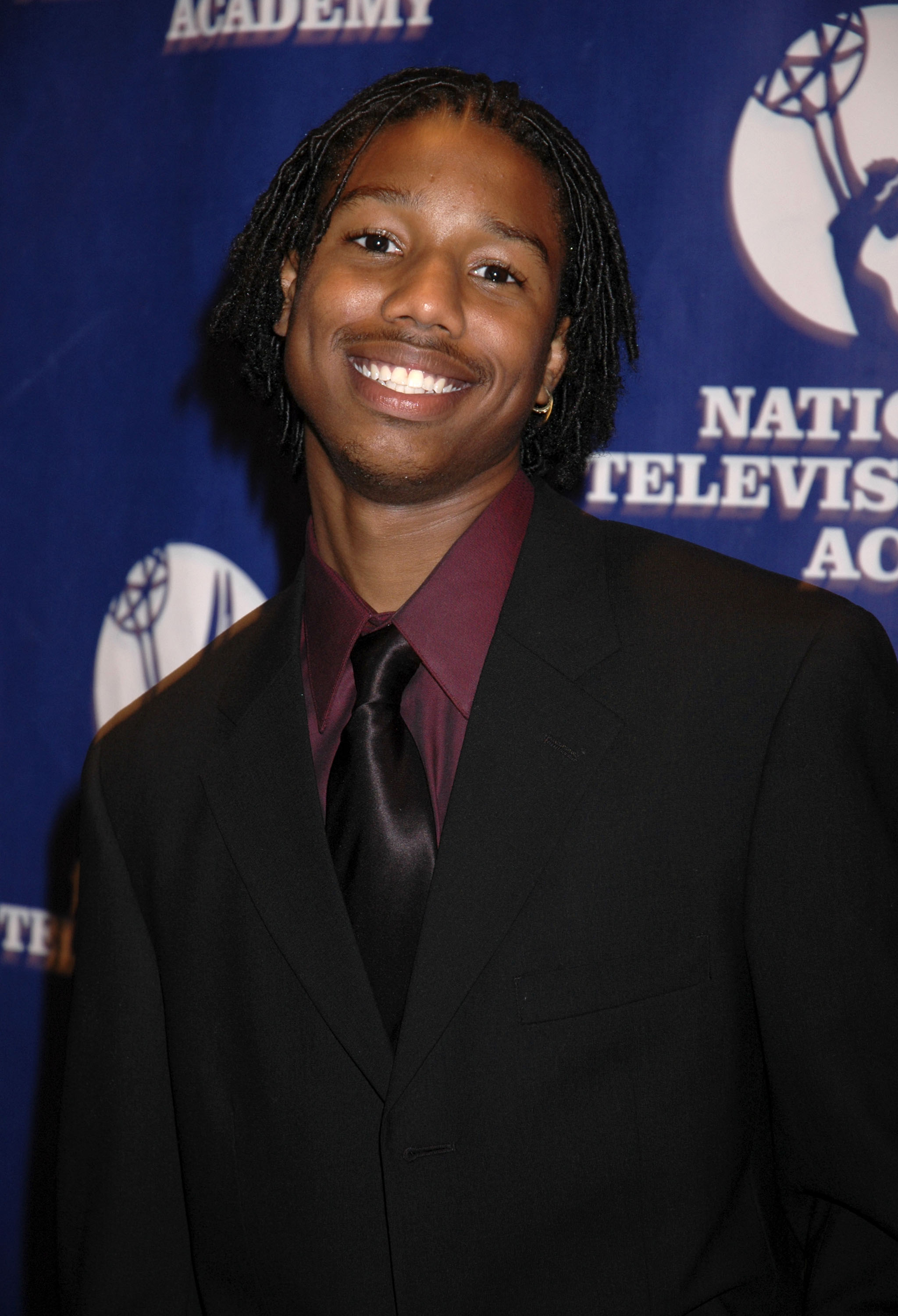 closeup of him wearing a large suit with shoulder length locs