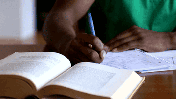 Person writing notes beside open books on a table, focused on the task