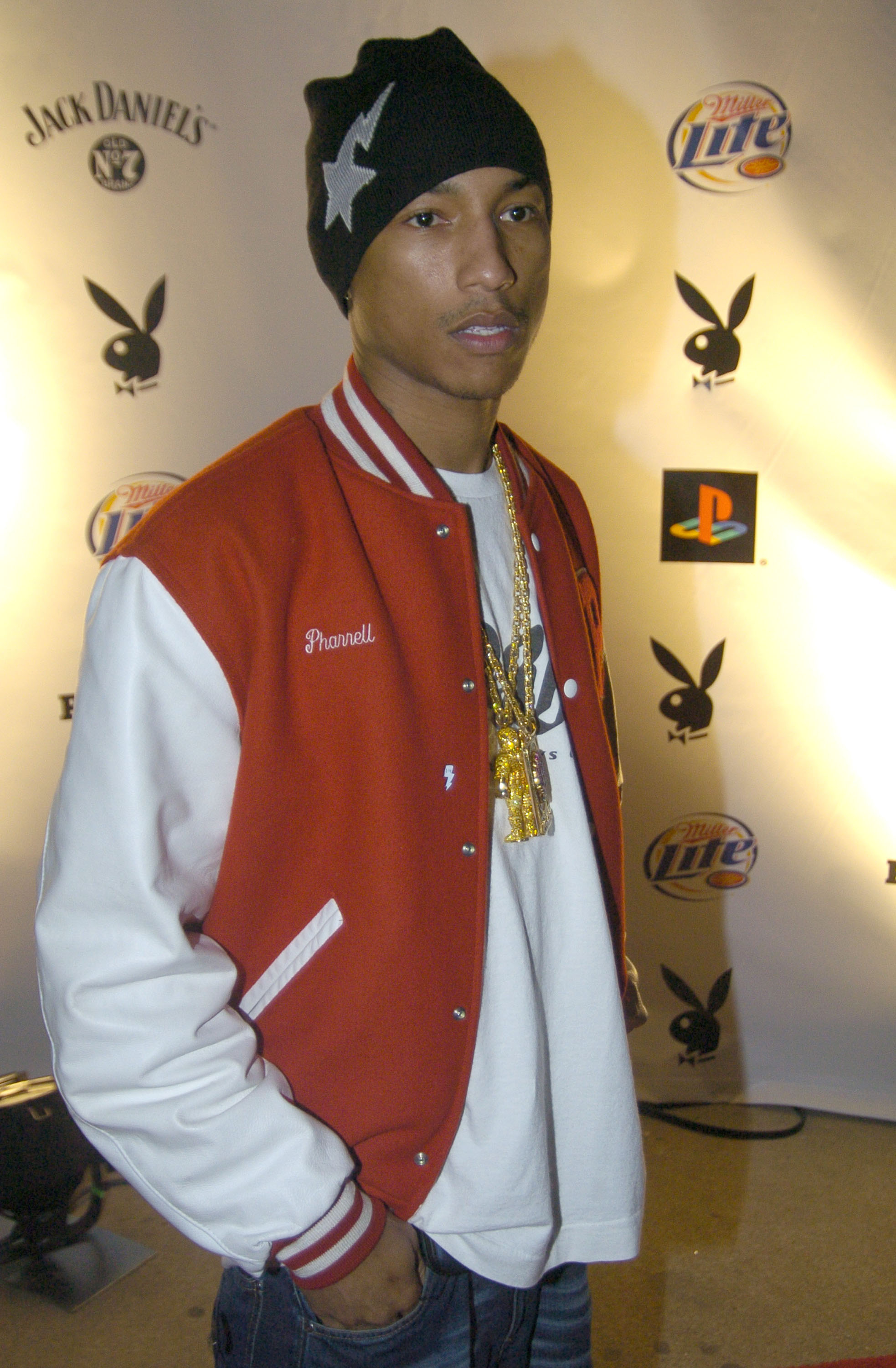a younger pharrell in a letterman style jacket and a beanie with large gold necklaces