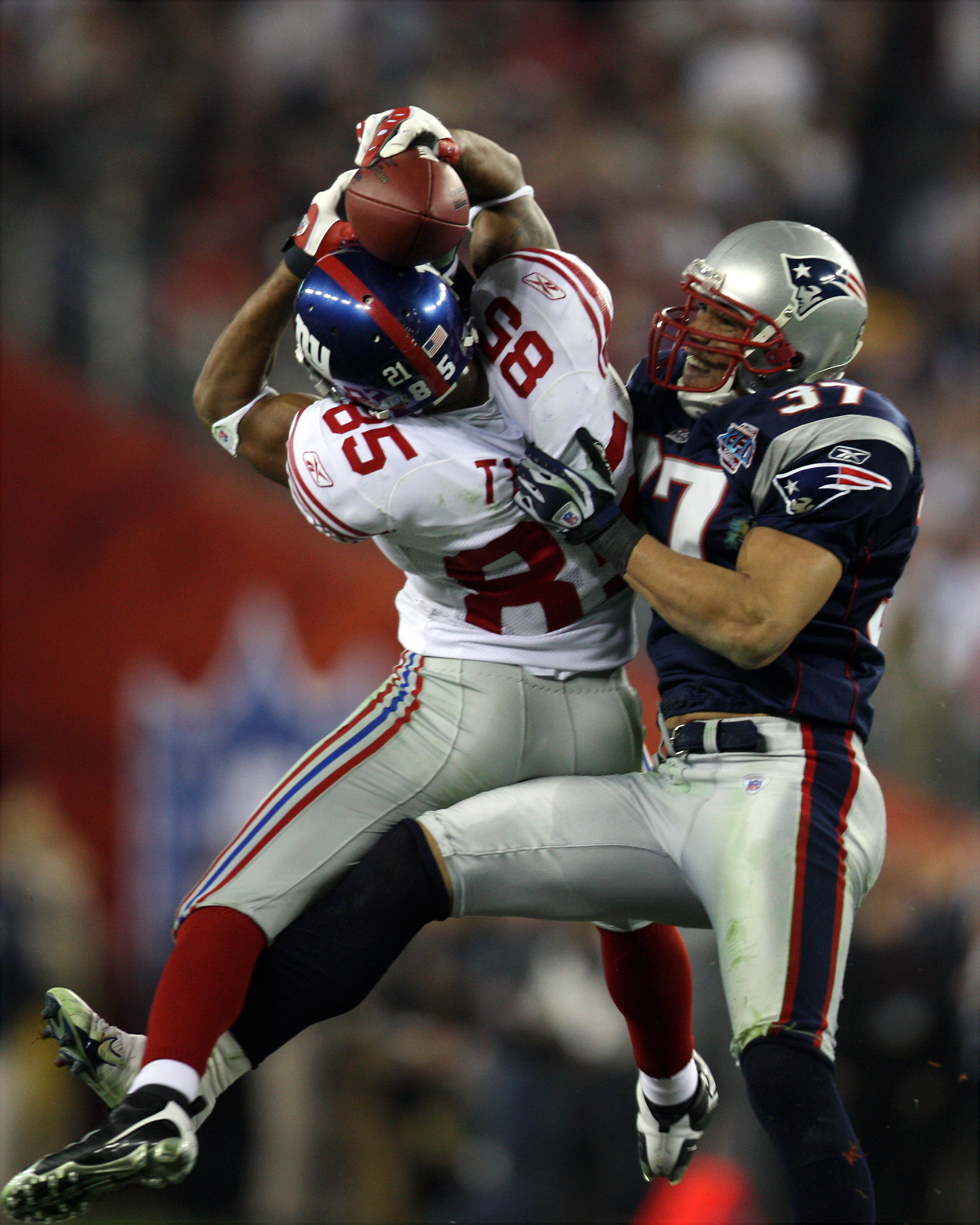 player catching the ball mid-air while a patriot goes in for a tackle