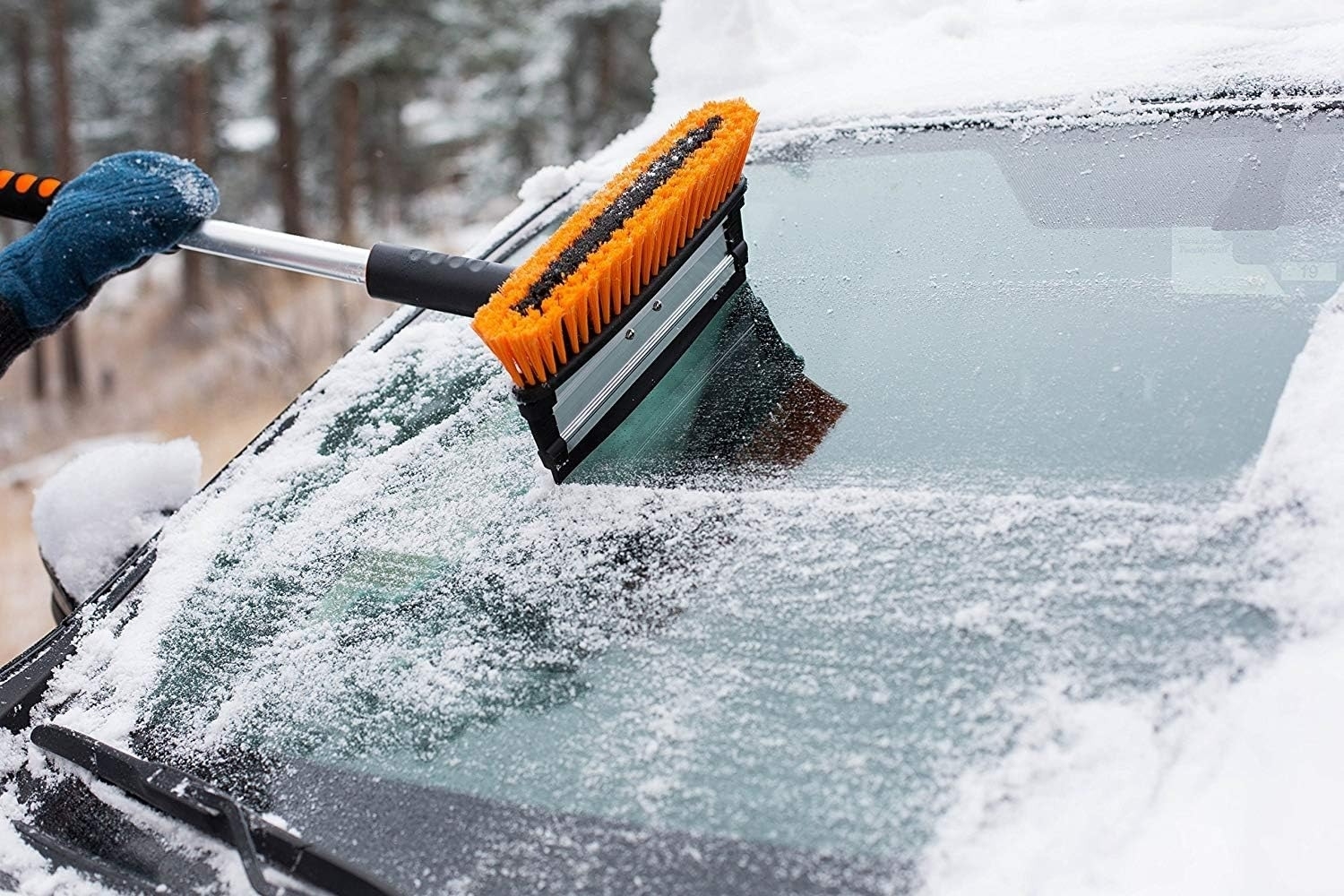 a person using the brush on their snowy windshield