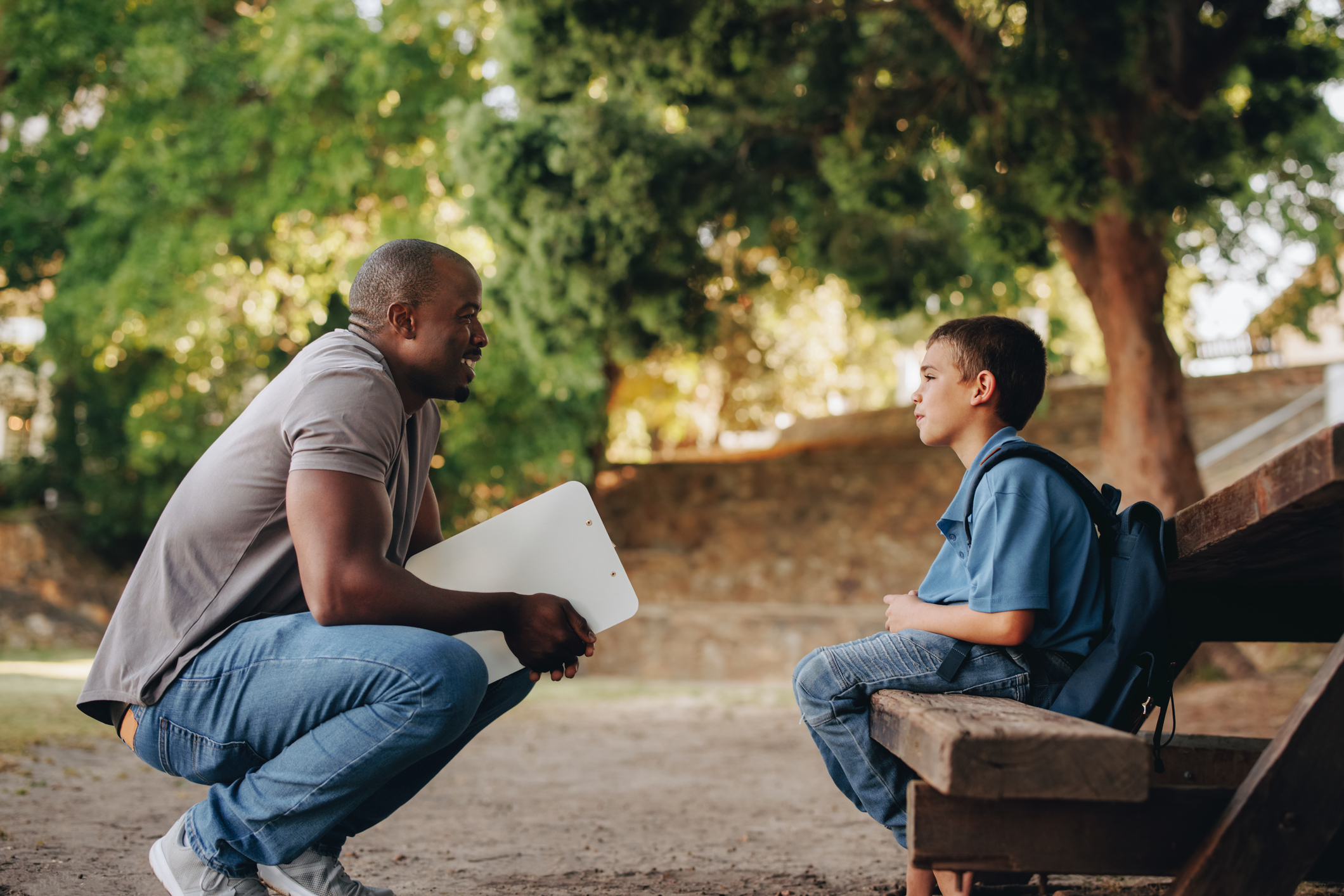 Male teacher talking to sad boy elementary school student