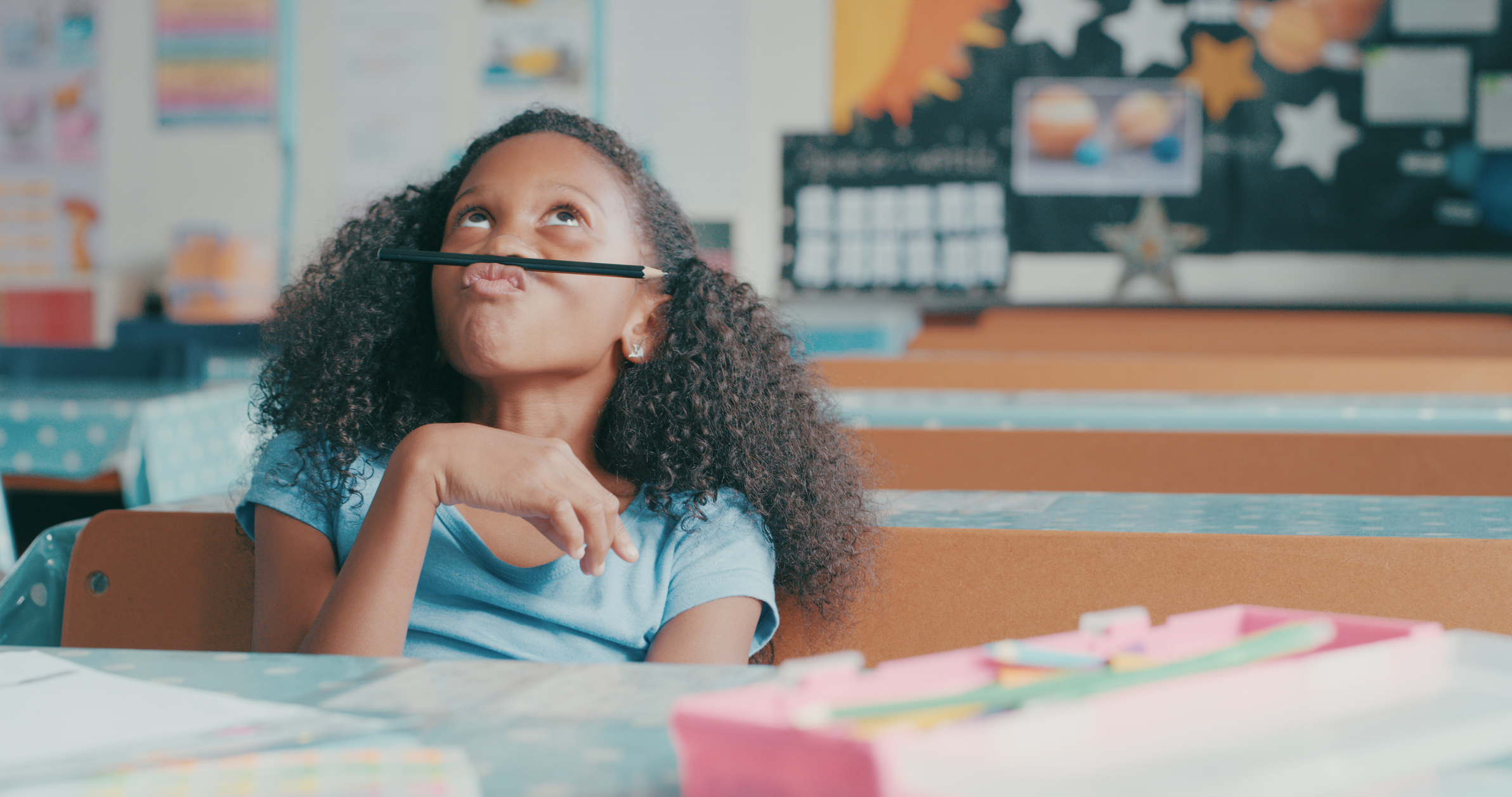 little girl holding a pencil above her lips with a careless expression
