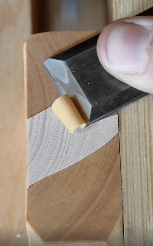 Close-up of a person peeling paper off wood with a knife