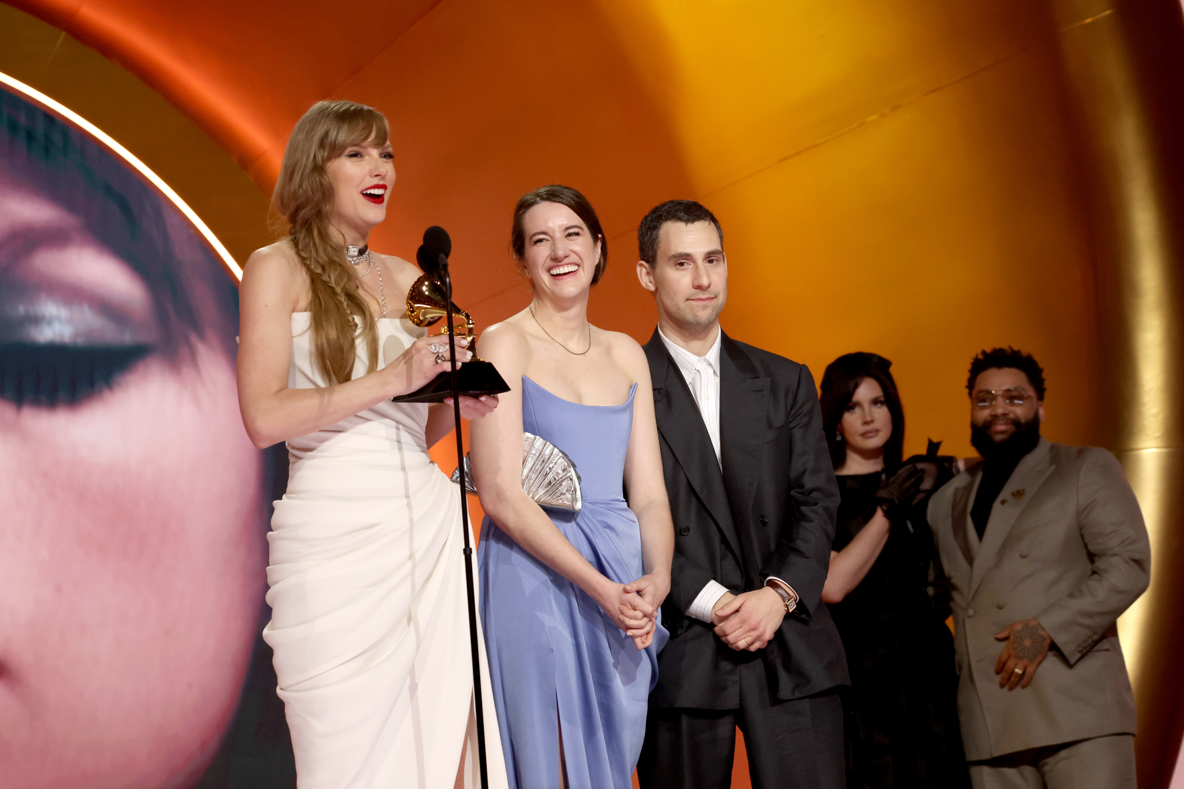 Close-up of Taylor onstage holding a Grammy with Lana and others behind her