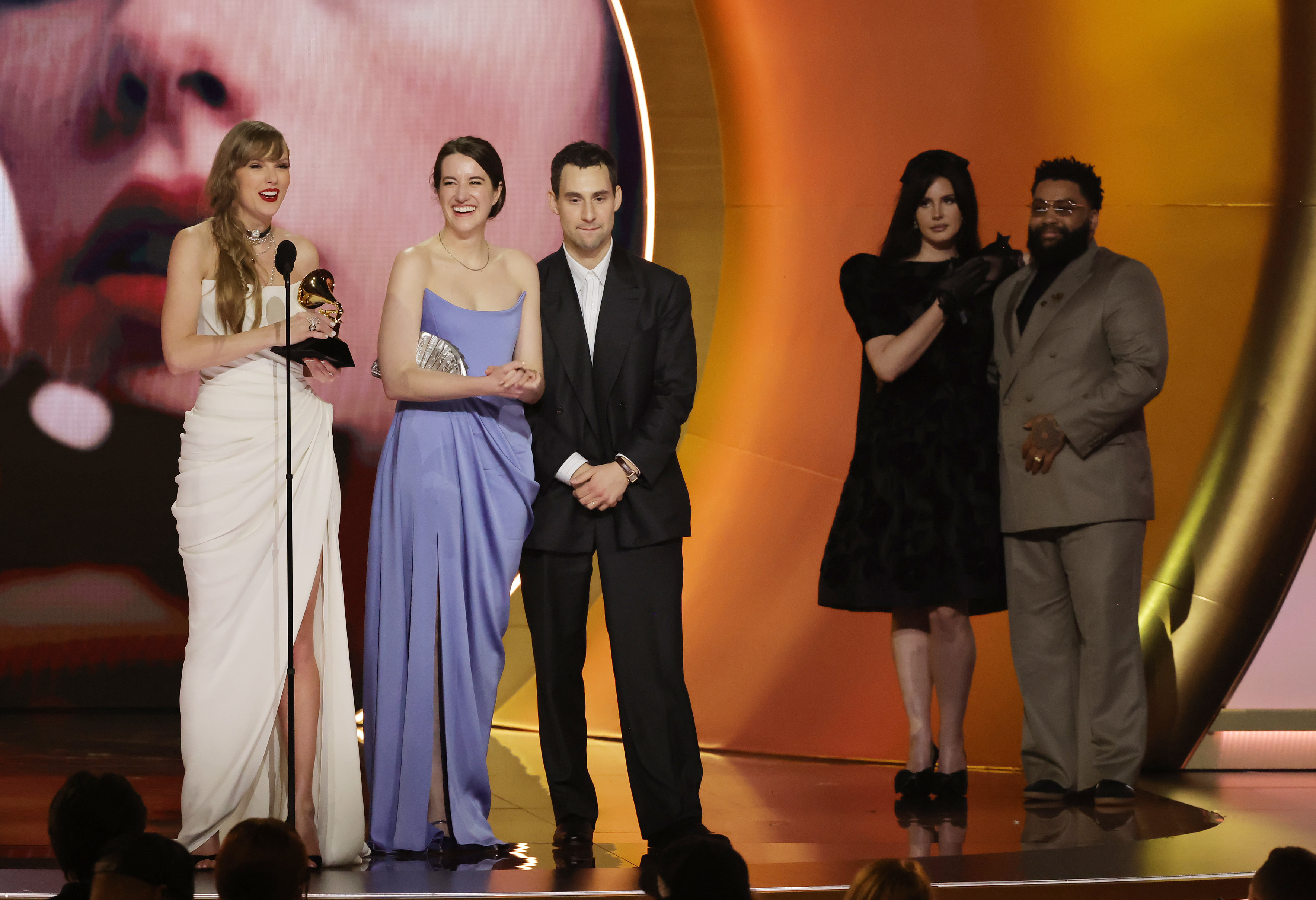 Close-up of Taylor onstage holding a Grammy, with Lana and others behind her