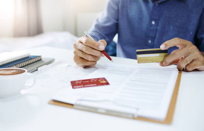 person holding credit card over a clipboard with various paper on top of it