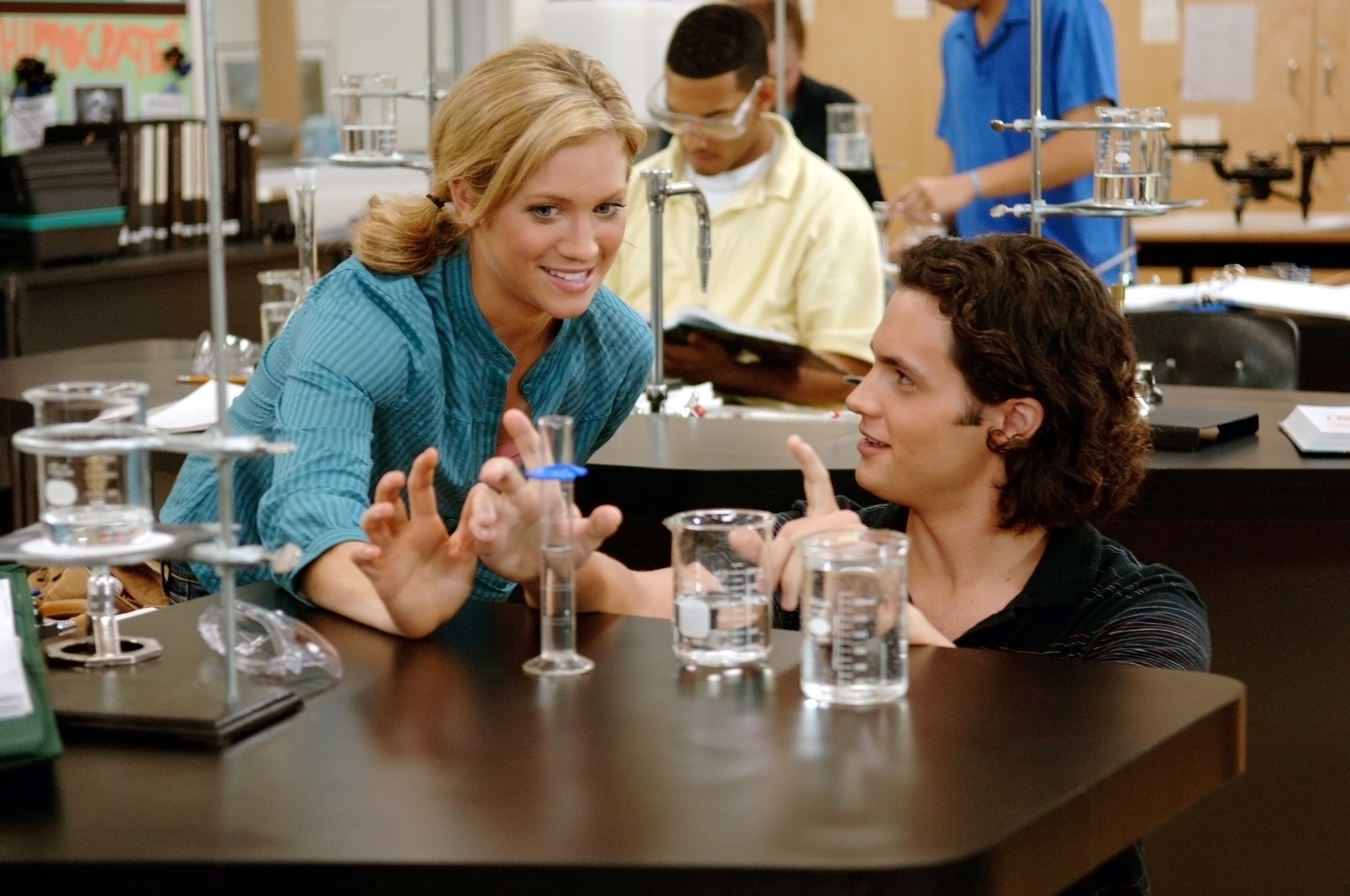 Brittany Snow and Penn Badgley at a science desk.