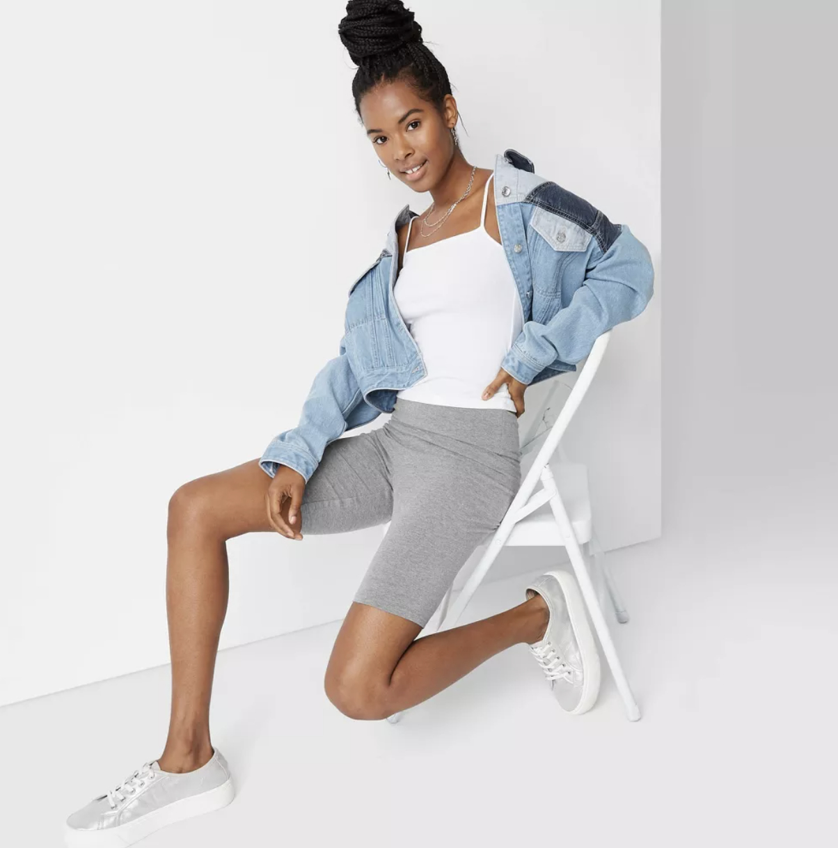 model sitting in a chair wearing a denim jacket, white top, grey skirt, and white sneakers