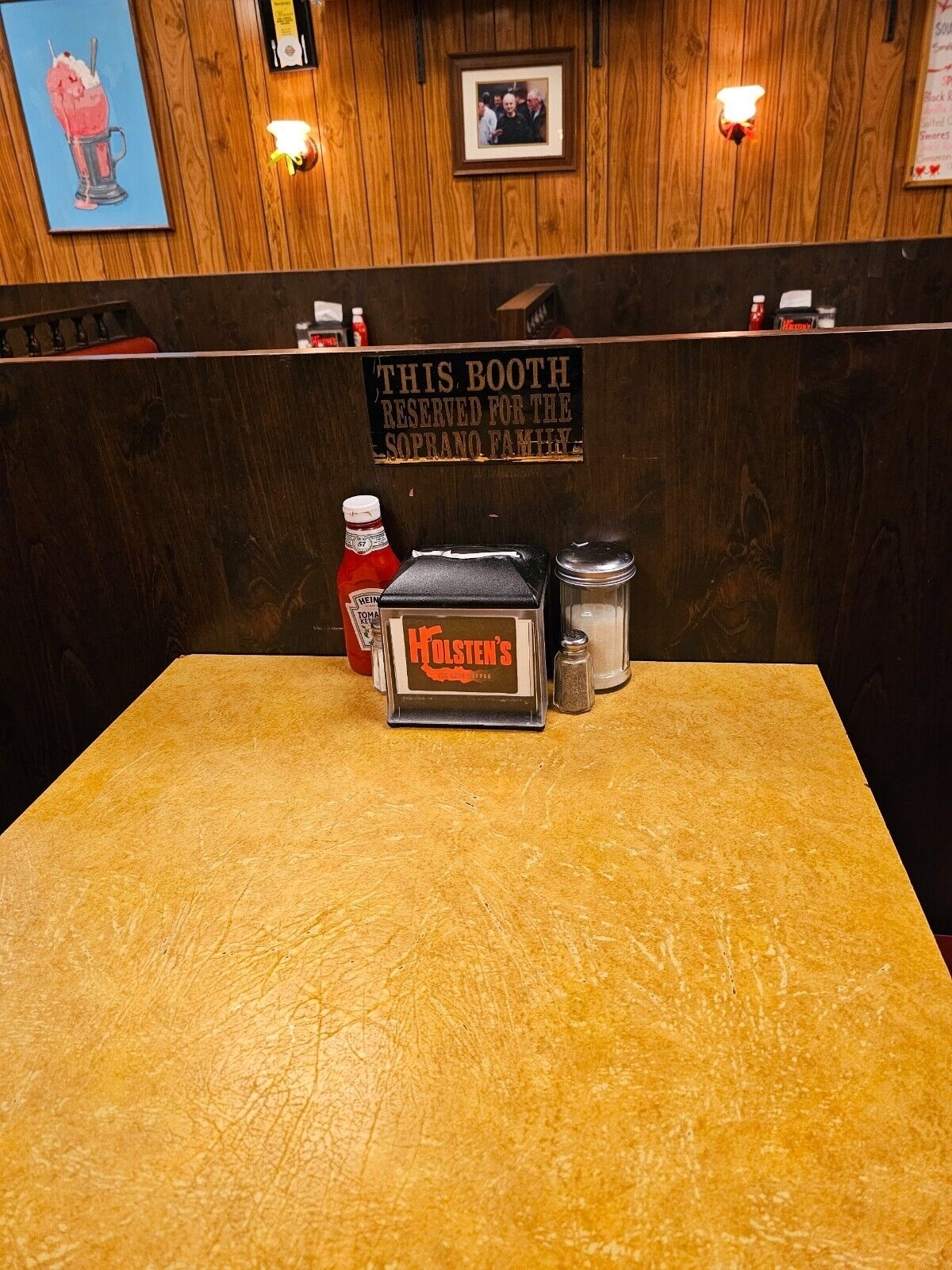 A diner booth with a sign stating &quot;THIS BOOTH RESERVED FOR THE SOPRANO FAMILY,&quot; with condiments on the table