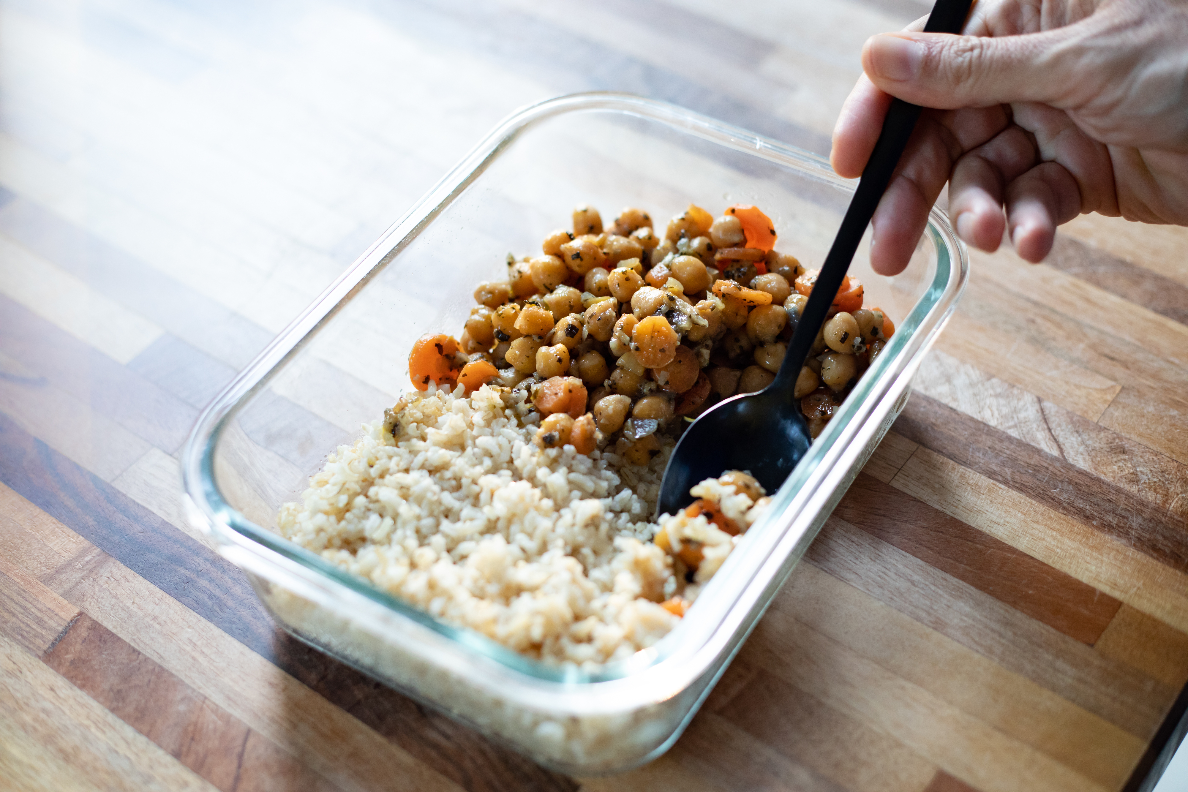 Meal-prep concept with chickpeas, carrots, and rice in a glass container being eaten with a fork