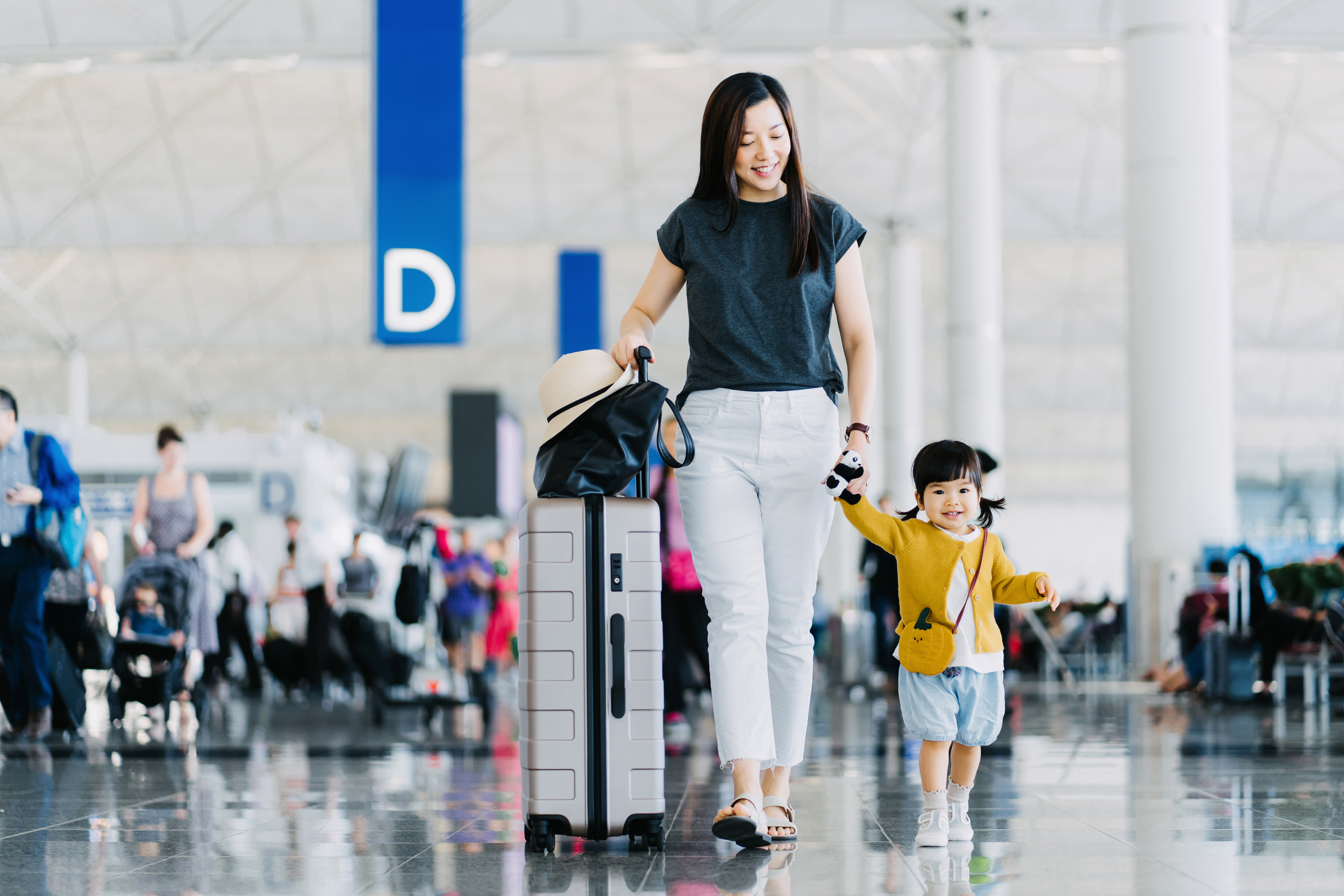 Woman and child walking in airport, holding hands, child smiling and carrying a small backpack