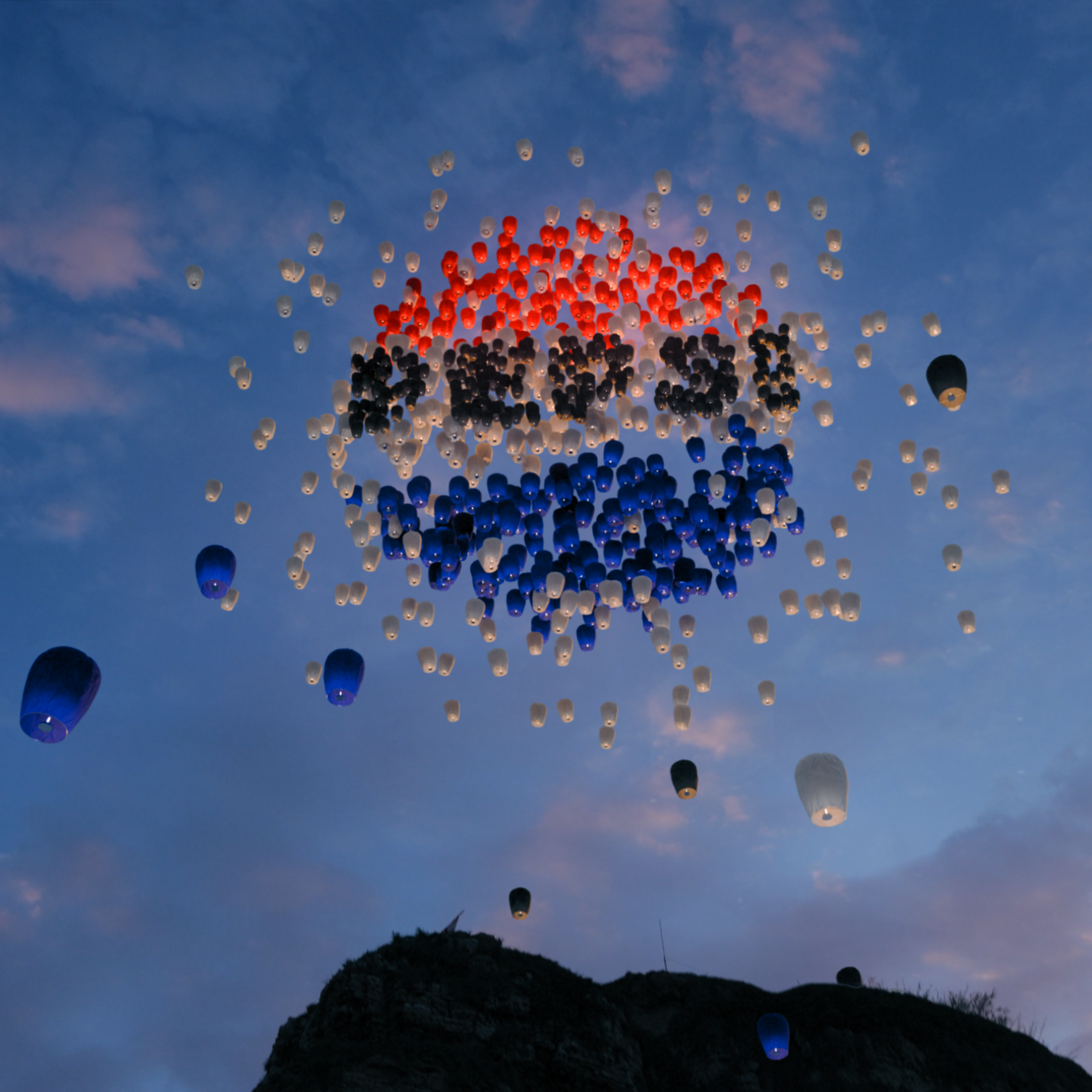A sunset sky with numerous balloons creating a colorful pattern above a silhouette of a hill