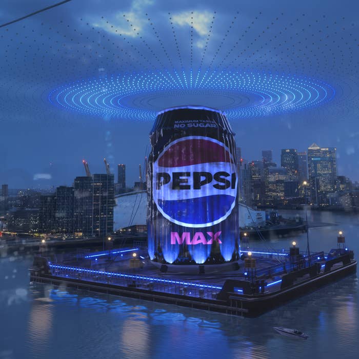 A Pepsi Max can-shaped structure is displayed on a barge at night with a city skyline background and illuminated patterns above