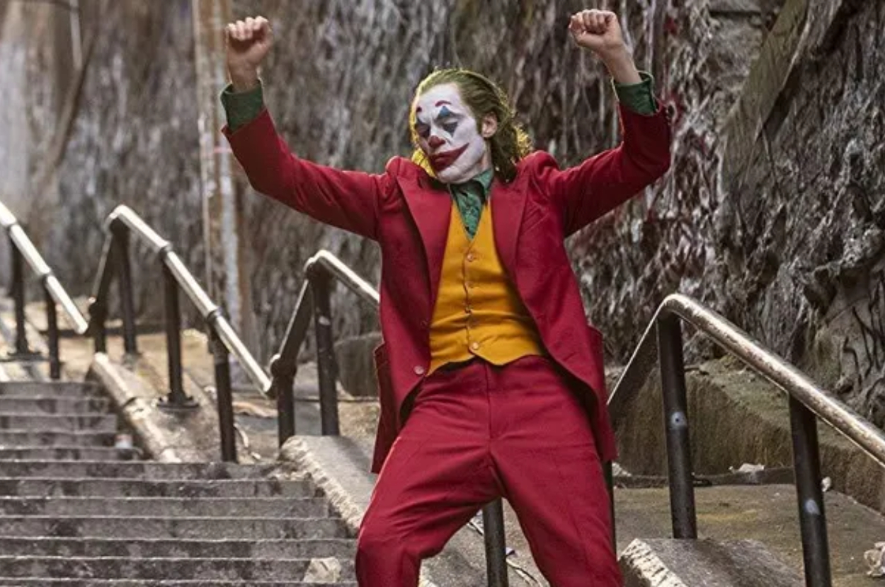 Joker character in red suit dancing triumphantly on stairs