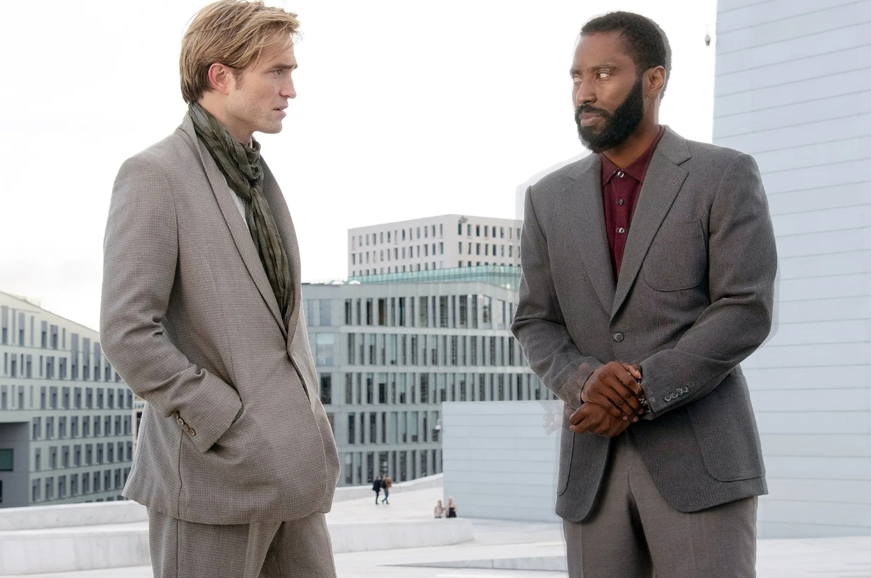 Two men in suits stand talking with serious expressions in an outdoor setting