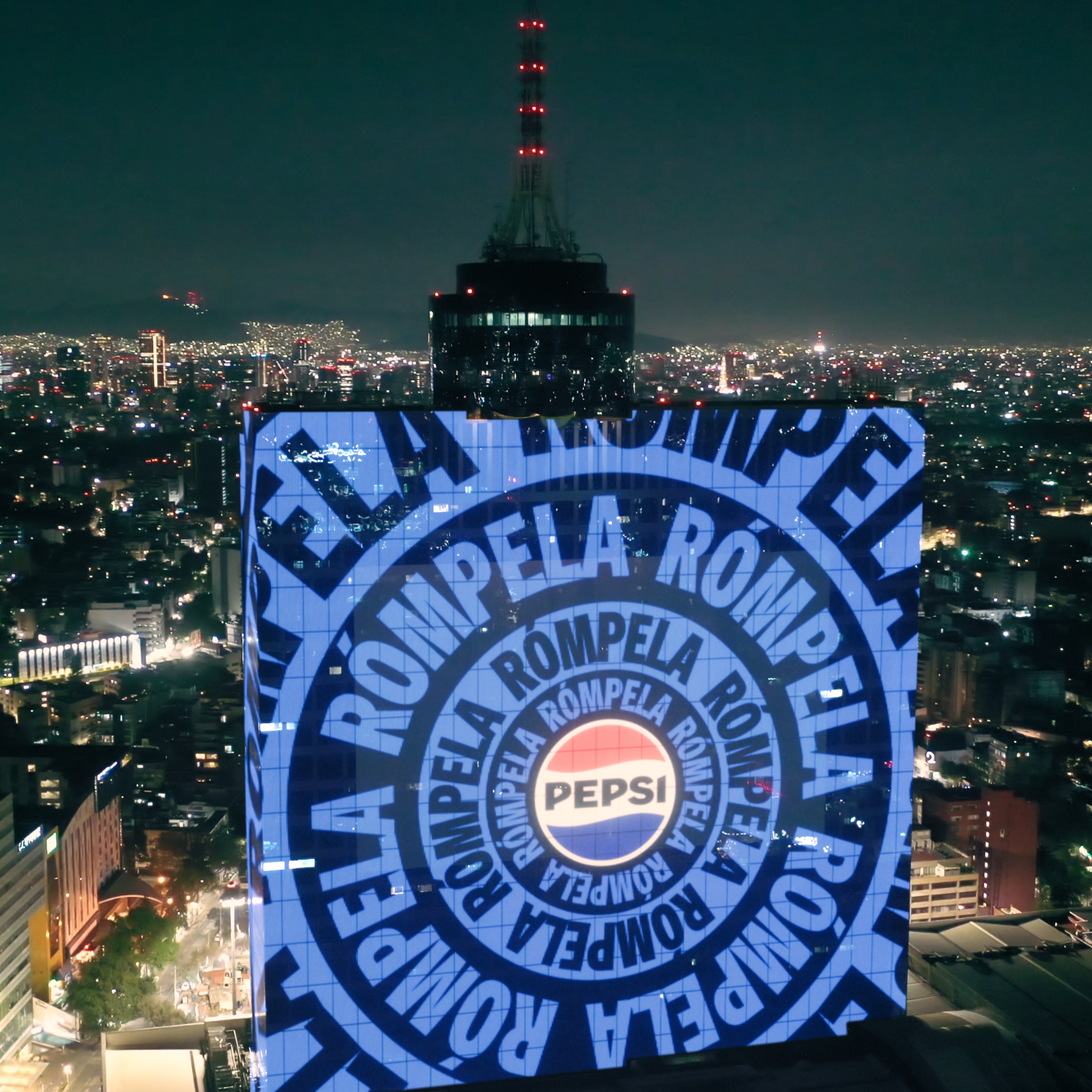 Billboard with Pepsi logo and repeated text &quot;ROMPELA&quot; in cityscape at night