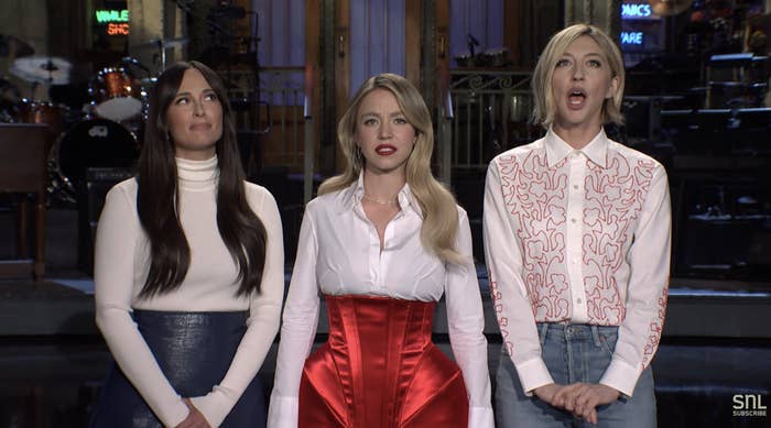 The three women on SNL stage: Sydney in a corset over a blouse,  Kacey and Heidi in long-sleeved tops