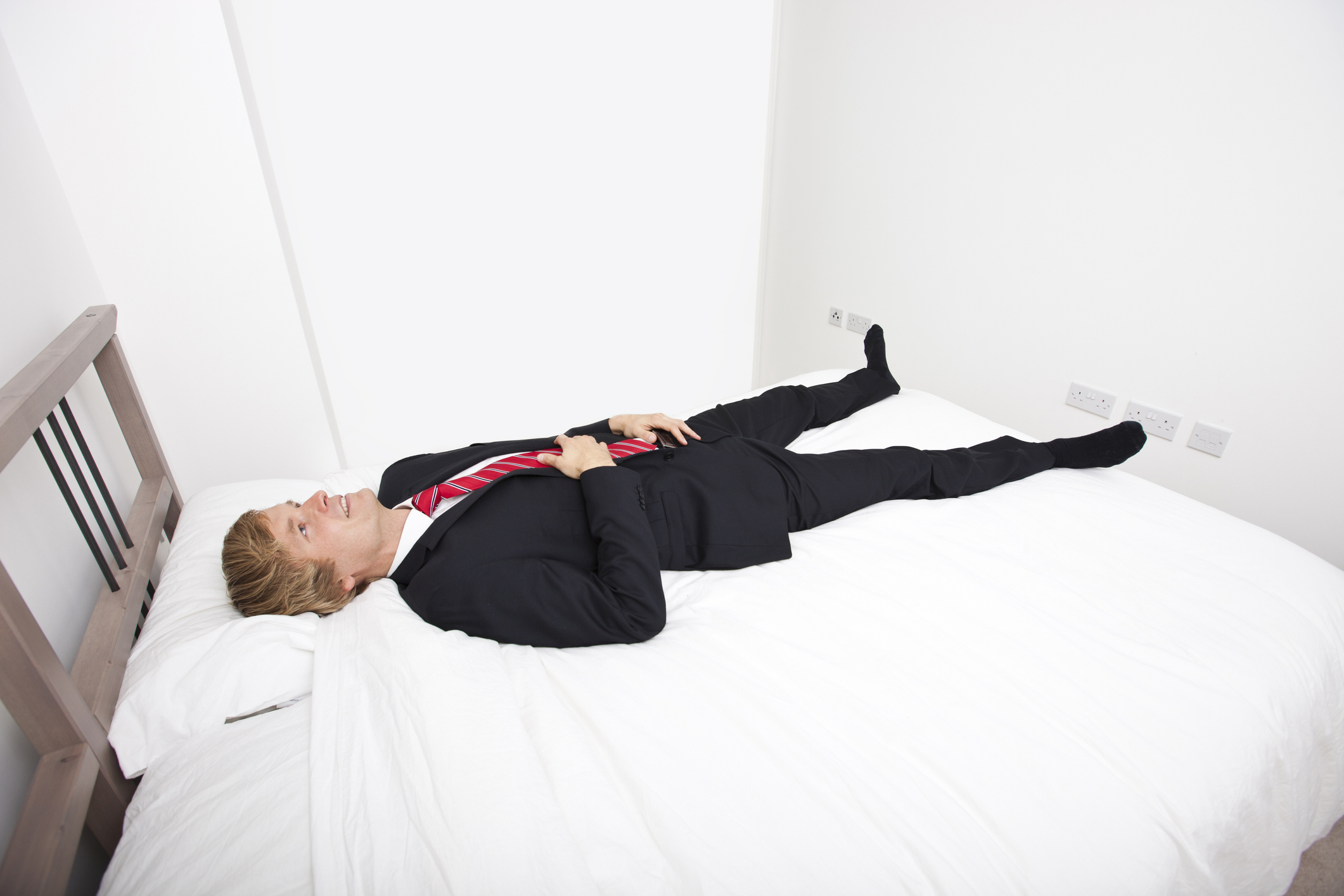 Person in a suit lying on a bed with one leg raised, looking upward