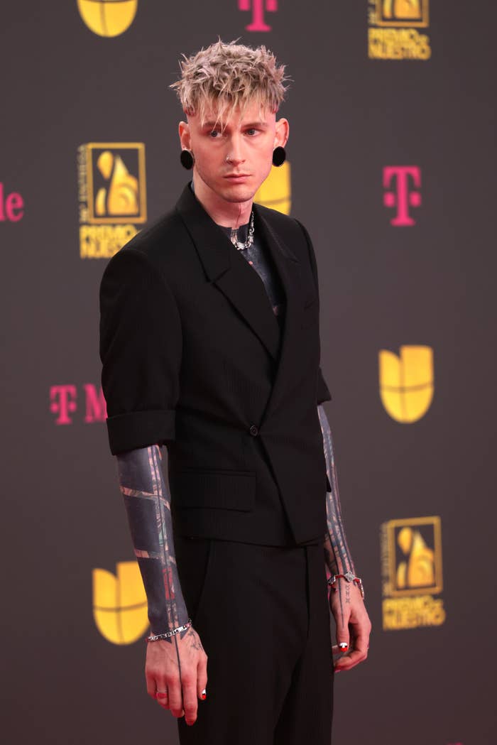 Machine Gun Kelly in a suit showing off his sleeves of tattoos posing on the event red carpet