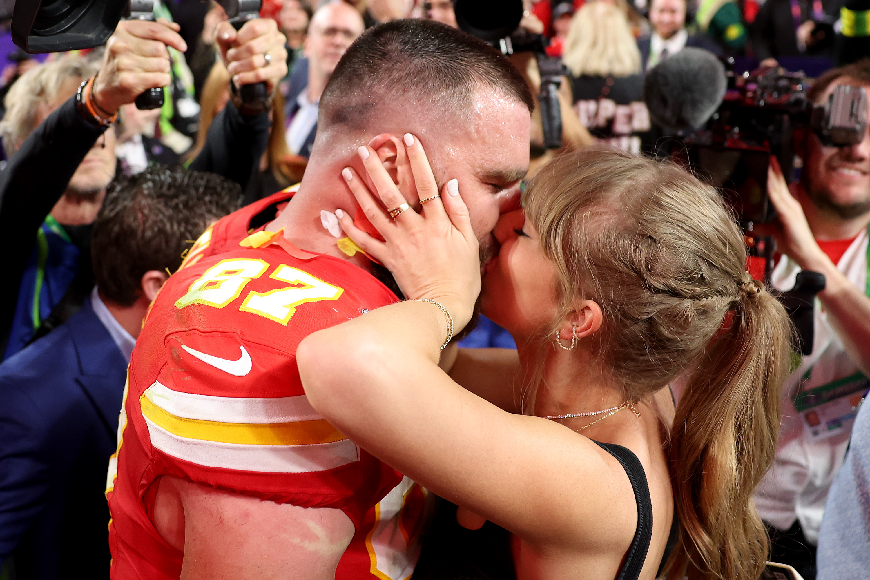 Person in a sports jersey number 87 shares a kiss with a person amidst a crowd with cameras