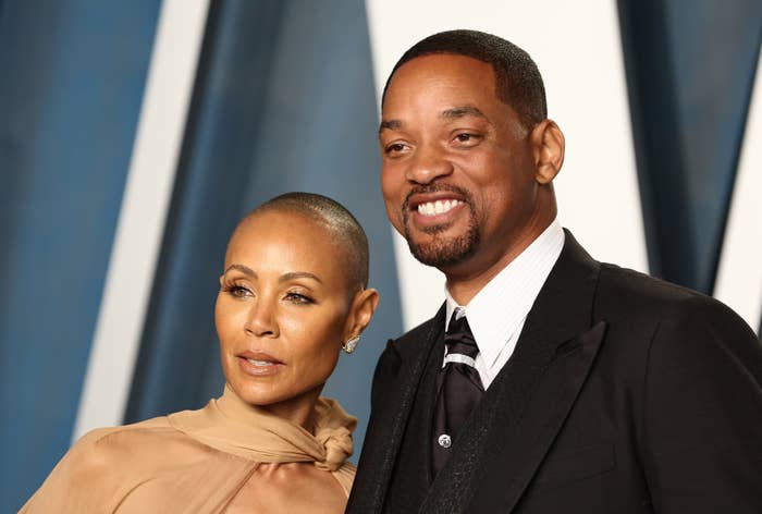 Jada in a high-neck gown and Will in a suit with a lapel pin at a media event