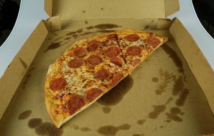 Half-eaten pepperoni pizza inside an open box with visible grease stains