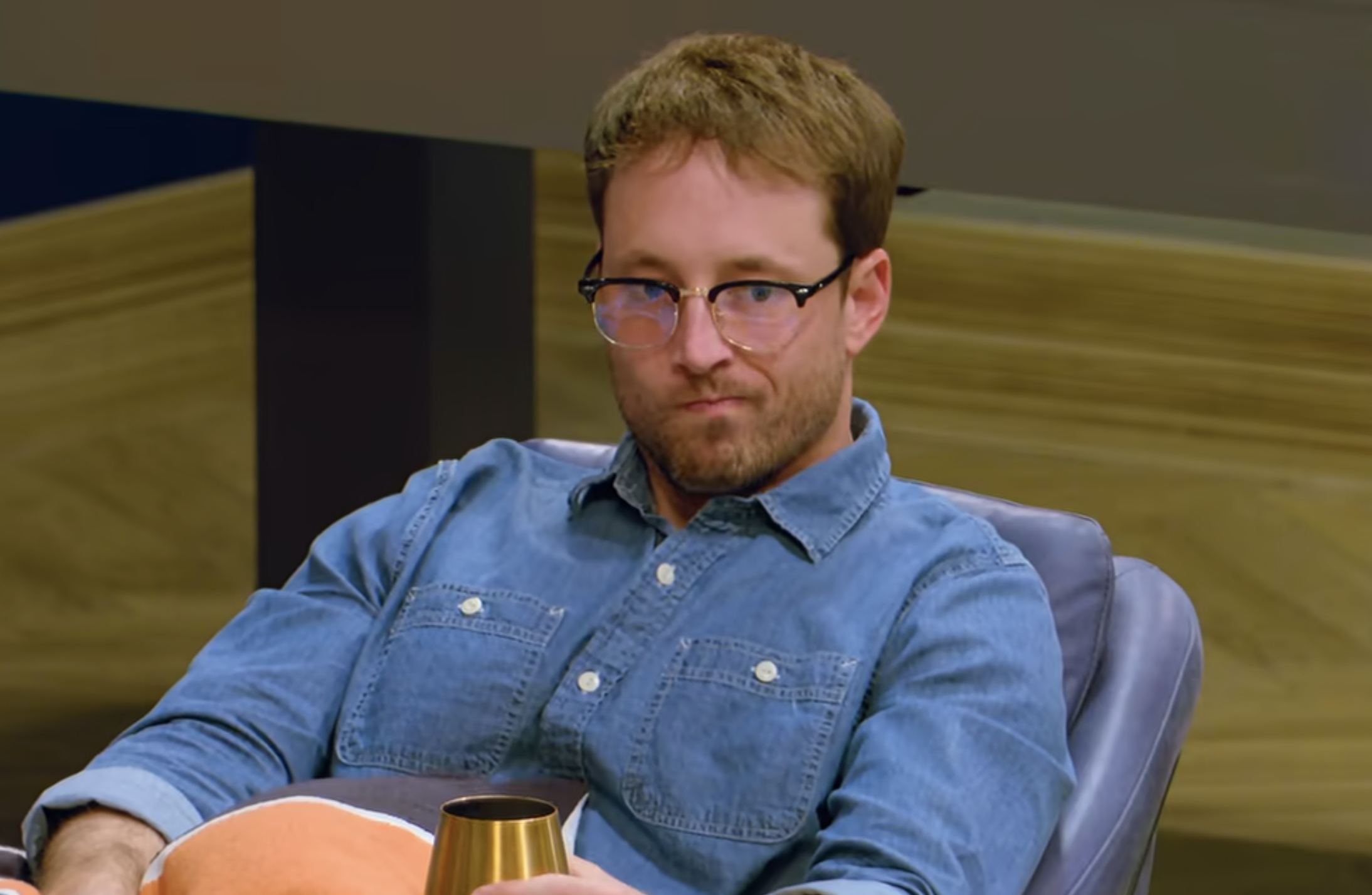 Jeremy in a denim shirt sitting with a cup, looking off into the distance