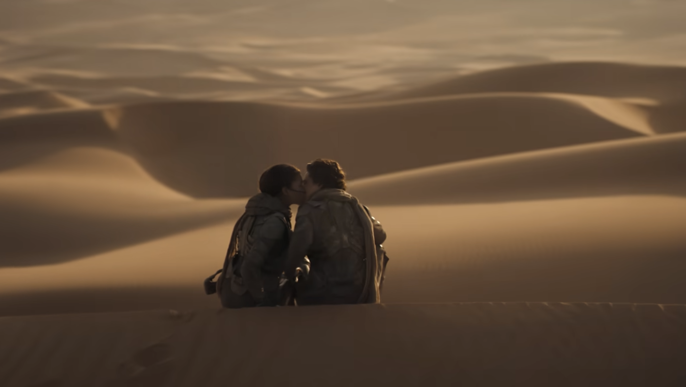 Dos personajes se besan en un desierto de dunas en una escena de película o serie de TV