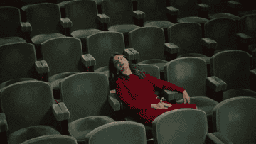 Mujer en vestido rojo sentada sola en un teatro vacío, parece cansada o frustrada