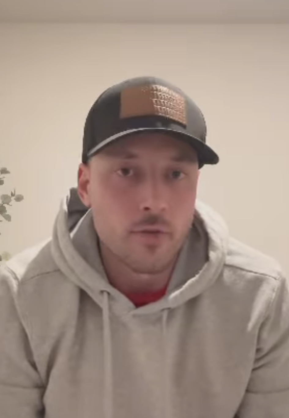 Jeremy in a cap and hoodie sits in front of a computer, looking into the camera, with a pensive expression