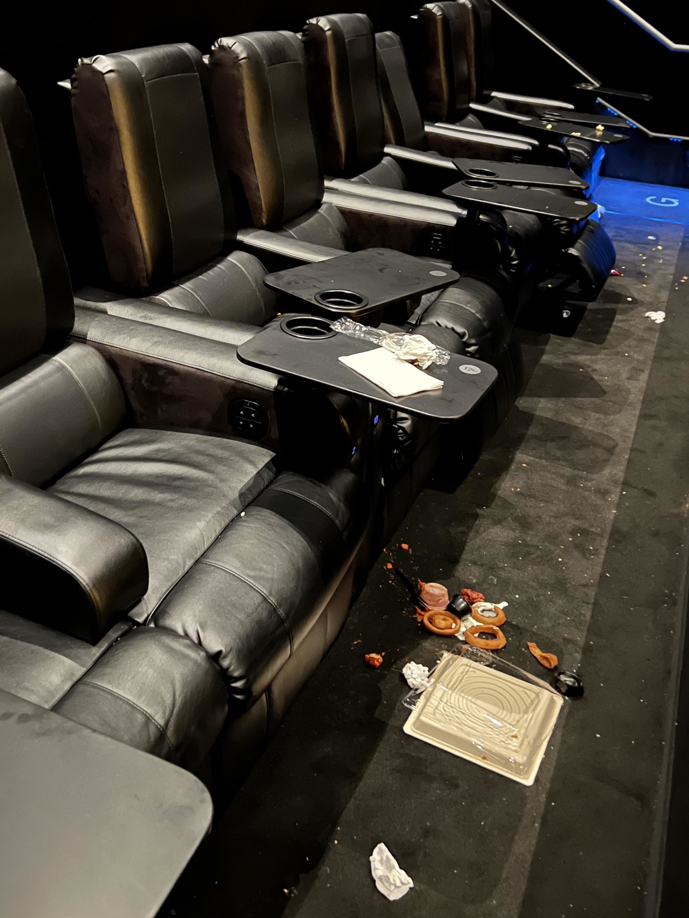 Messy cinema seating with discarded food and paper waste on the floor