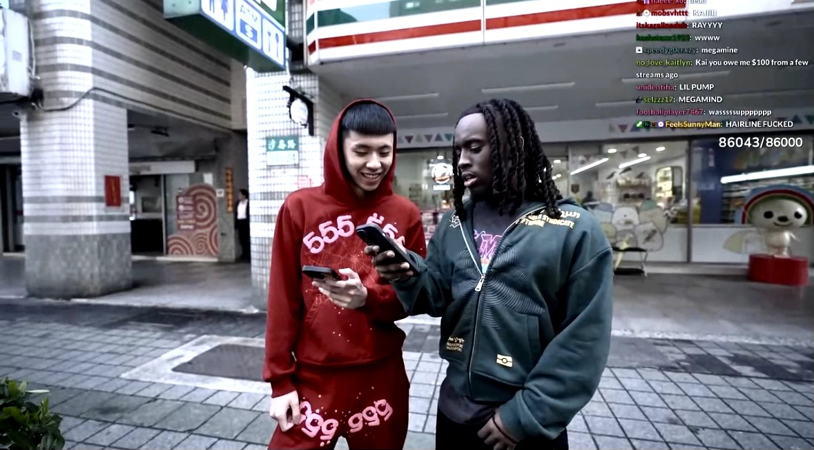 Two people standing together looking at a smartphone, one wearing a red hoodie, the other in a green jacket